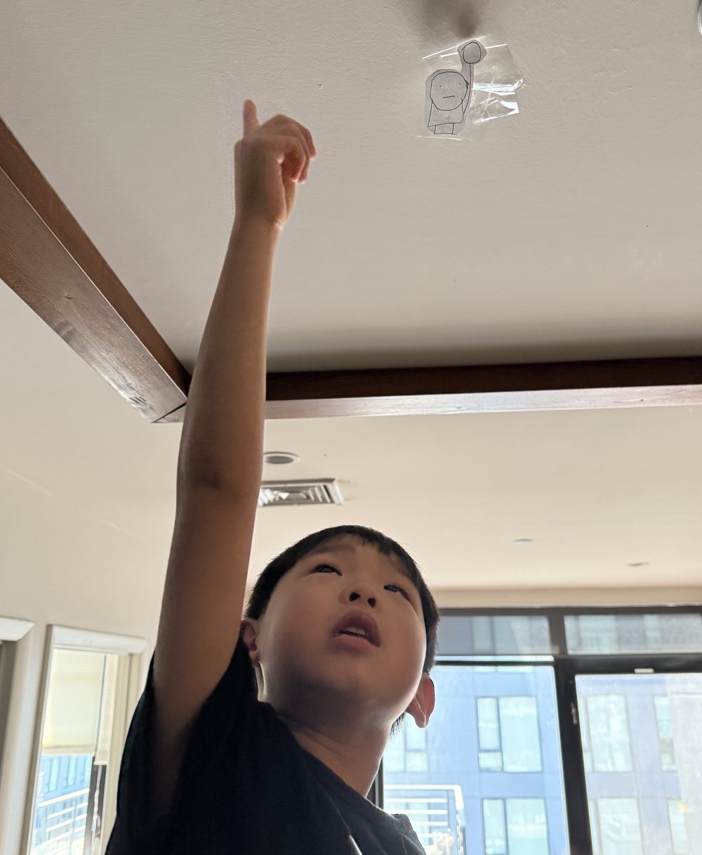 Beckham pointing at his drawing taped to the ceiling